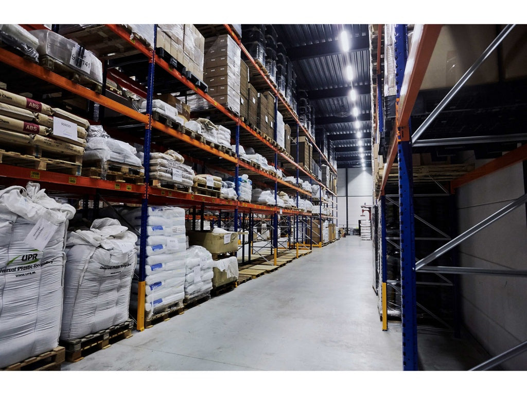 Lagergång med lagerhyllor, högt till tak. i taket sitter det armaturer med T5 lysrör.