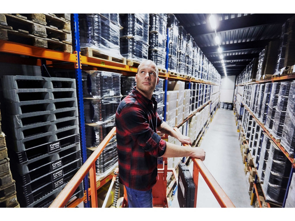 En man står i en skylift på ett lager redo att byta lysrör t5 mot LED-Lysrör T5.