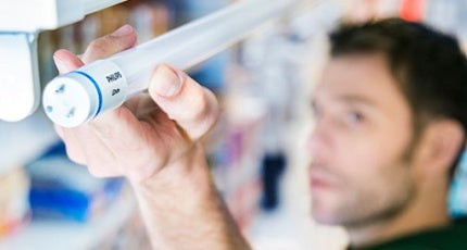 Man står och håller upp ett led-lysrör mot en lysrörsarmatur. Han ska precis sätta i LED lysröret och tittar mot änden av LED-Lysröret och av armaturen.